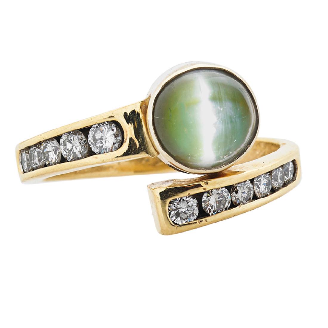 CAT'S EYE CHRYSOBERYL, DIAMOND & YELLOW GOLD RING: A round synthetic cat's eye chrysoberyl bezel set between bypass of channel set RBC diamonds, approx. .90 ct. TW. 14k. Size 7 3/4. 3.3 dwt.