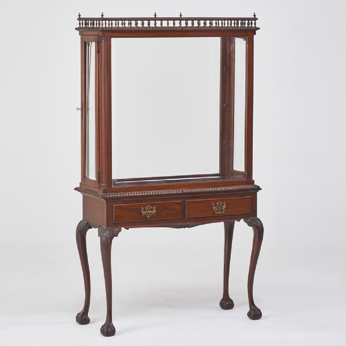 CHIPPENDALE STYLE: Vitrine on stand with carved gallery top, fluted apron, and two drawers raised on carved cabriole legs terminating with ball and claw feet, late early 20th c. Mahogany, beveled glass, brass Unmarked 6
