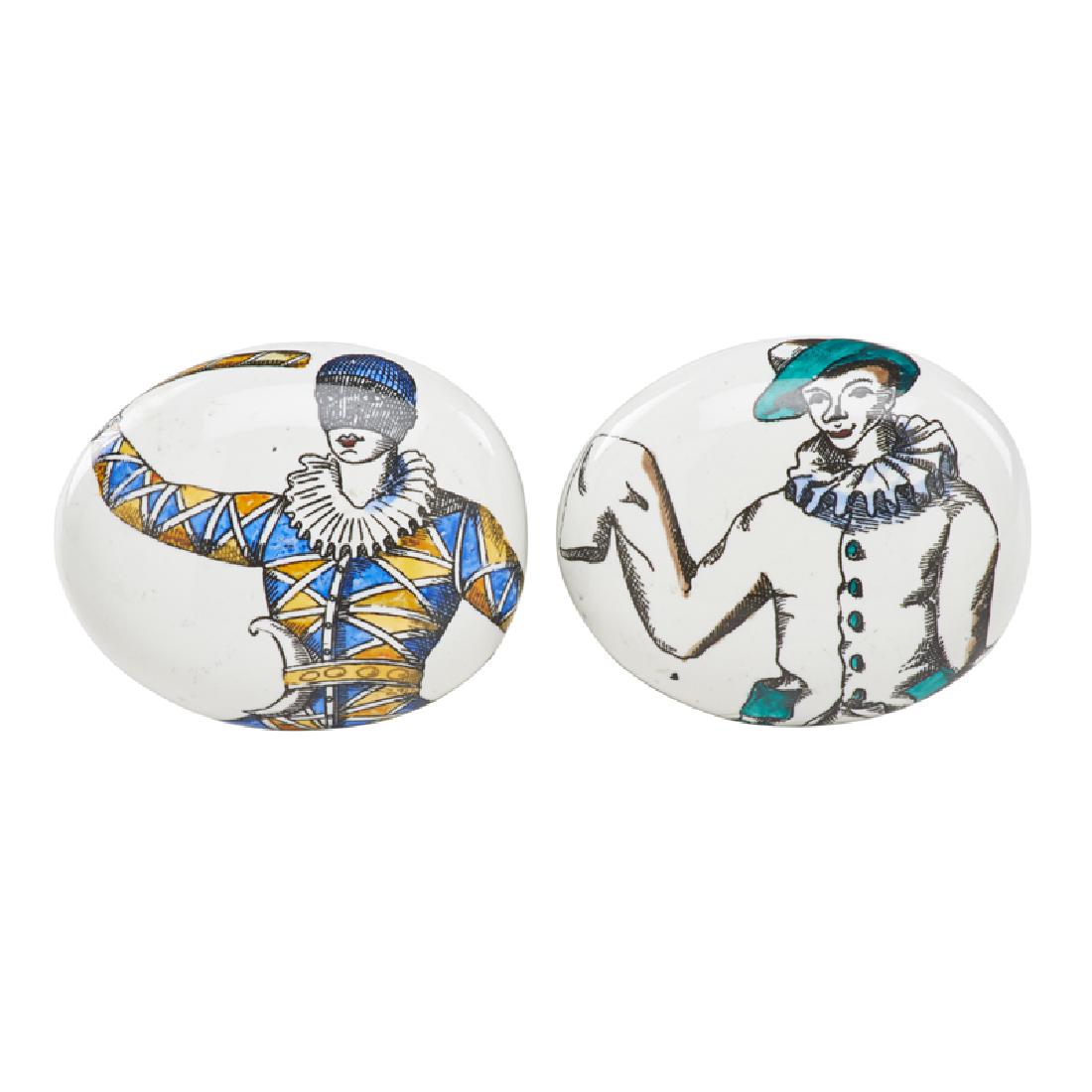 PIERO FORNASETTI: Two "pebble" paperweights with characters from the Commedia dell'arte, Italy, 1970s Hand-painted porcelain Both marked 1 1/2" x 3 3/4" x 3"