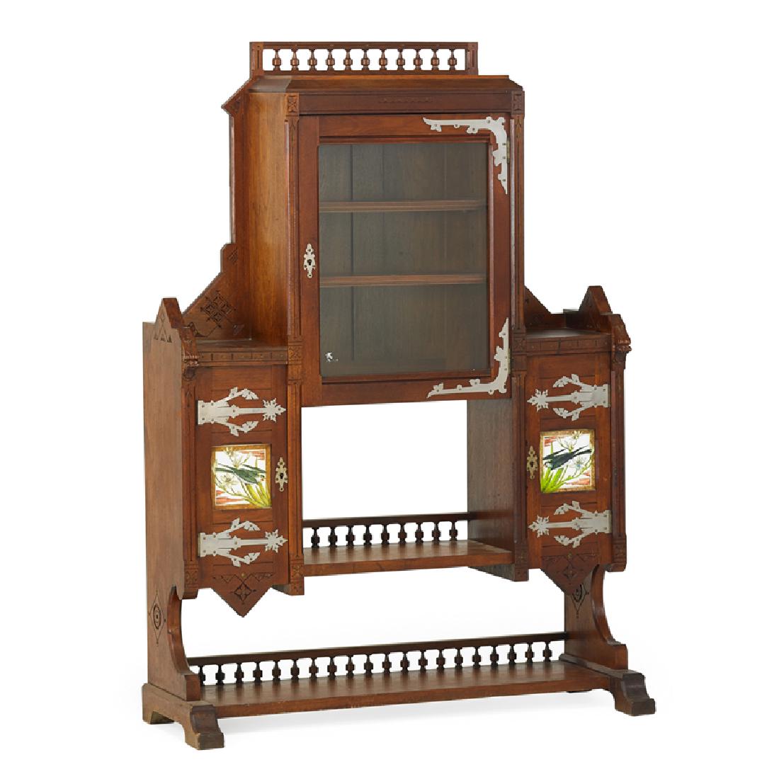KIMBEL & CABUS BOOKCASE: Modern Gothic design, carved walnut, metal fittings, pottery, USA, ca. 1880 Tiles marked "Simpson & Sons" 60 1/2" x 42 1/2" x 16" Reference: Furniture designed and sold by the New York firm of Kimbel 
