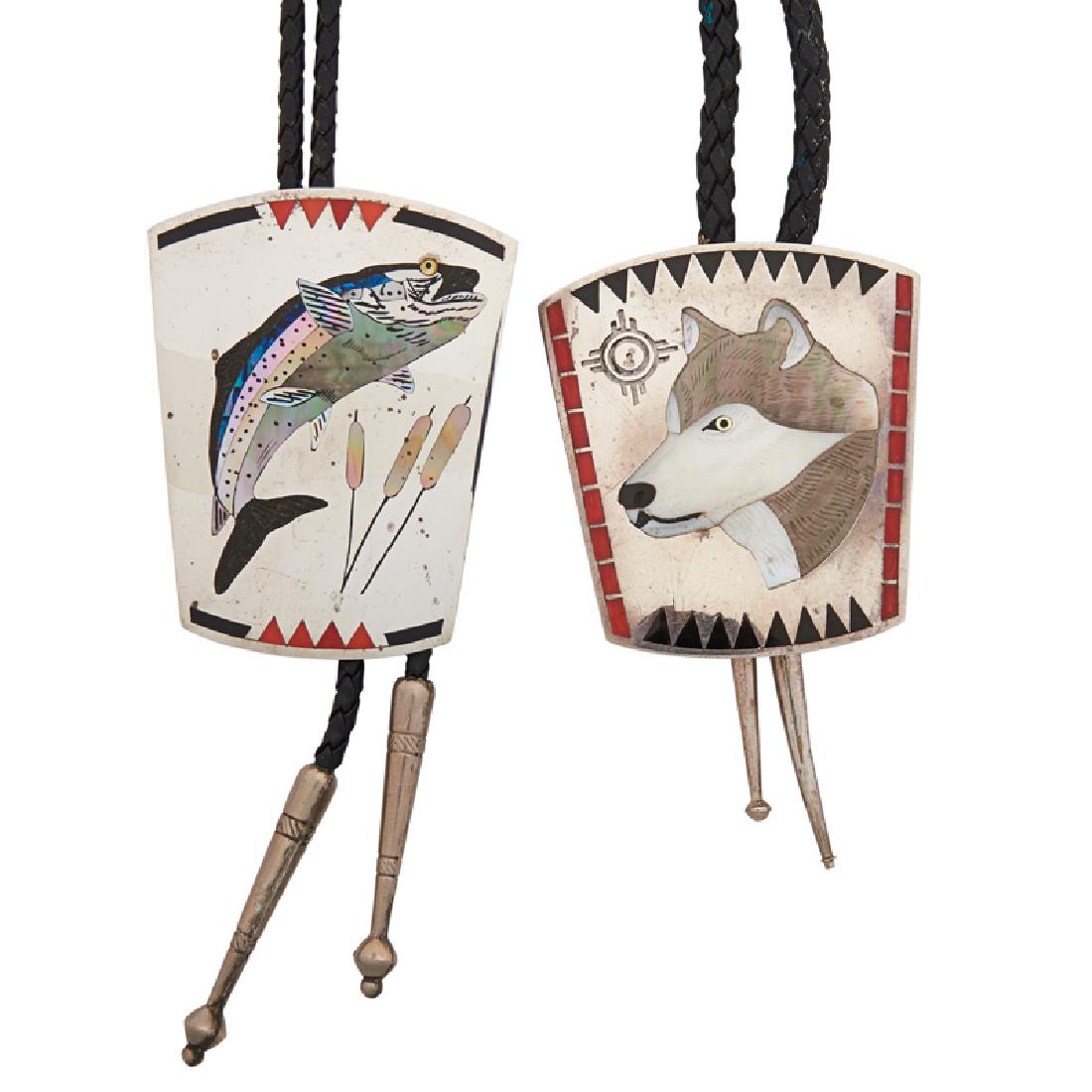 EDAAKIE HARDSTONE INLAID SILVER BOLO TIES: The two Zuni bolos with mother-of-pearl, coral an onyx inlaid trout by Dale Edaakie or wolf's head by Dennis and Nancy Edaakie, on braided leather cord terminating in engraved silver. Stamped by the m