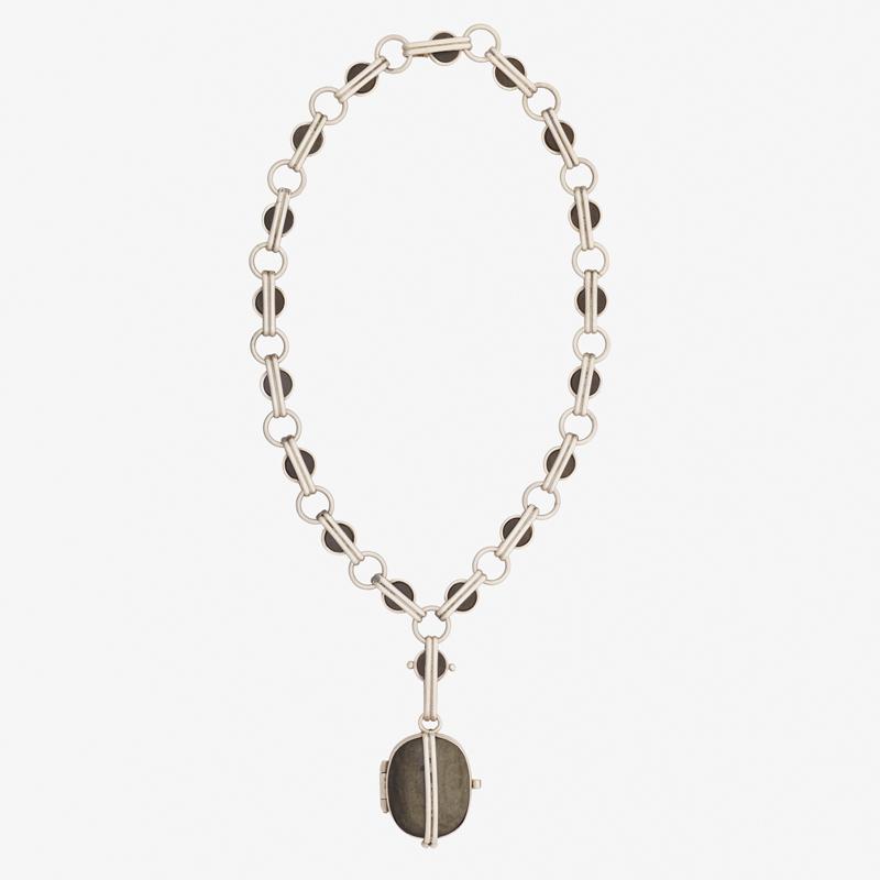 WILLIAM SPRATLING HARDSTONE & SILVER LOCKET NECKLACE: An obsidian disc and circle link chain suspends a carved obsidian cushion-shaped locket. 1962-1964. Stamped by the maker. 20", 3" drop. 126.4 gs.