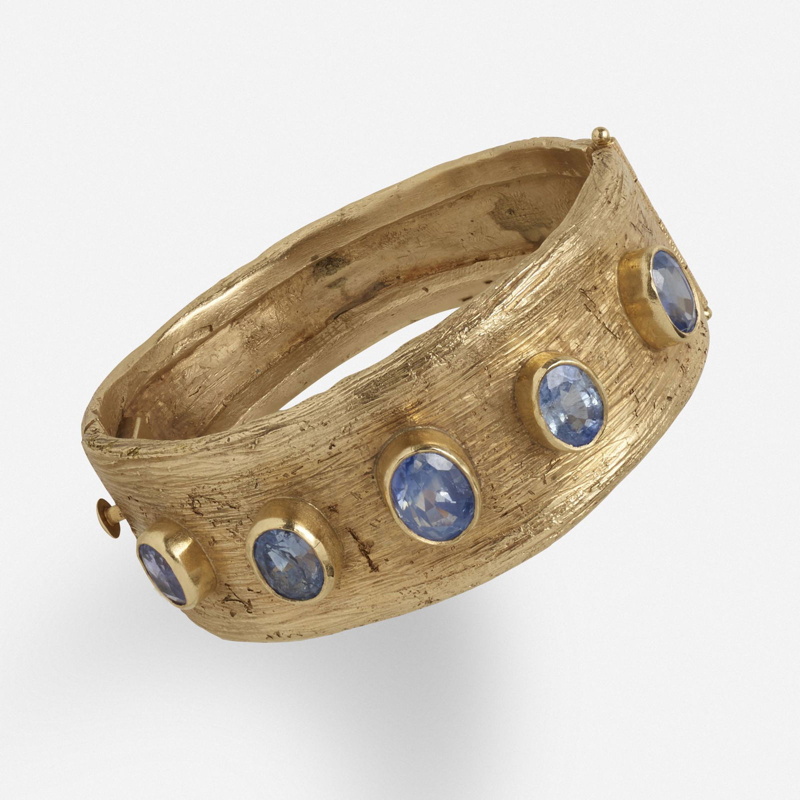 Ed Wiener, Modernist sapphire and gold bracelet: Ed Wiener Modernist sapphire and gold bracelet Textured gold hinged bangle bracelet, accented by five bezel-set sapphires 14k yellow gold Inner circ. 6 1/4 ins; Gross weight 40.8 dwts