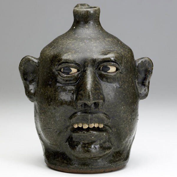 LANIER MEADERS Face jug: LANIER MEADERS Face jug with clay teeth covered in green ash glaze. Signed Lanier Meaders. 9''