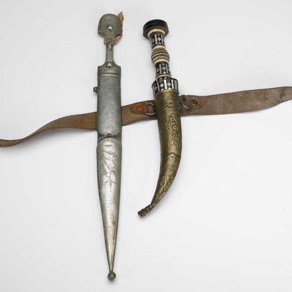 TWO DAGGERS: TWO DAGGERS; Kindjal with nickel silver mountings, 16''; Jambiya with ebony, ivory and mother-of-pearl handle with turquoise and coral set into the blade, brass sheath; Longer: