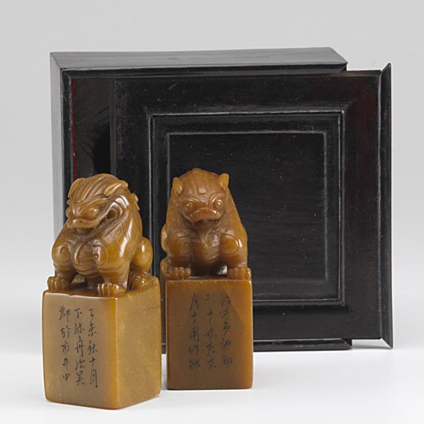 PAIR OF SOAPSTONE SEALS: PAIR OF SOAPSTONE SEALS; Similar pair of seated lions rest on the top of these matching, reverse ground seals, early 20th c.; With fitted box; 5''