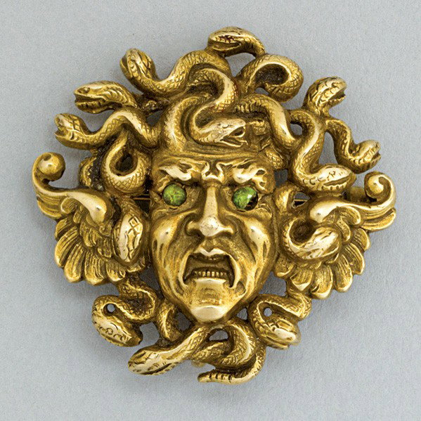 SCULPTED GOLD MEDUSA HEAD AND SERPENT BROOCH: SCULPTED GOLD MEDUSA HEAD AND SERPENT BROOCH, ca. 1900. Gustav Manz (attr.) in 14k with green garnet eyes, pendant hook on reverse. 4.73 dwt. (11 gs.), 1 1/8'' x 1 1/8''