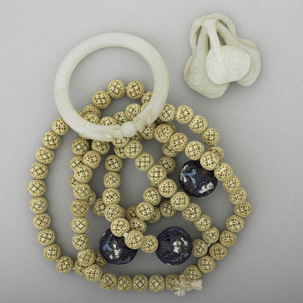QING DYNASTY IVORY BEADS AND CHINESE NEPHRITE: Strand of reticulated ivory beads,50", and three reticulated enameled beads with Champlevé iris blossoms; vegetal carved nephrite pendant, 2 1/2"; carved nephrite bangle in the form of confronted dra