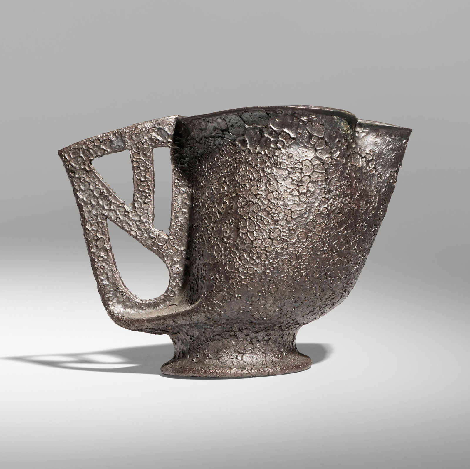 George E. Ohr, Pitcher: George E. Ohr Pitcher USA, 1897-1900 glazed earthenware 4.25 h x 5.75 w x 3 d in (11 x 15 x 8 cm) Pitcher features a lobed rim and cut-out handle with a volcanic gunmetal glaze. Impressed