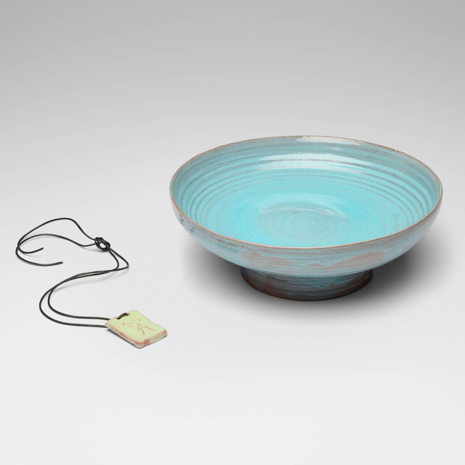 Beatrice Wood, Bowl; Necklace (two works): Beatrice Wood Bowl; Necklace (two works) c. 1980glazed earthenware, leather bowl: 3.75 h x 11 dia in (10 x 28 cm) pendant: 2 h x 1.5 w x 0.025 d in (5 x 4 x 0 cm) Slip signature to each exa