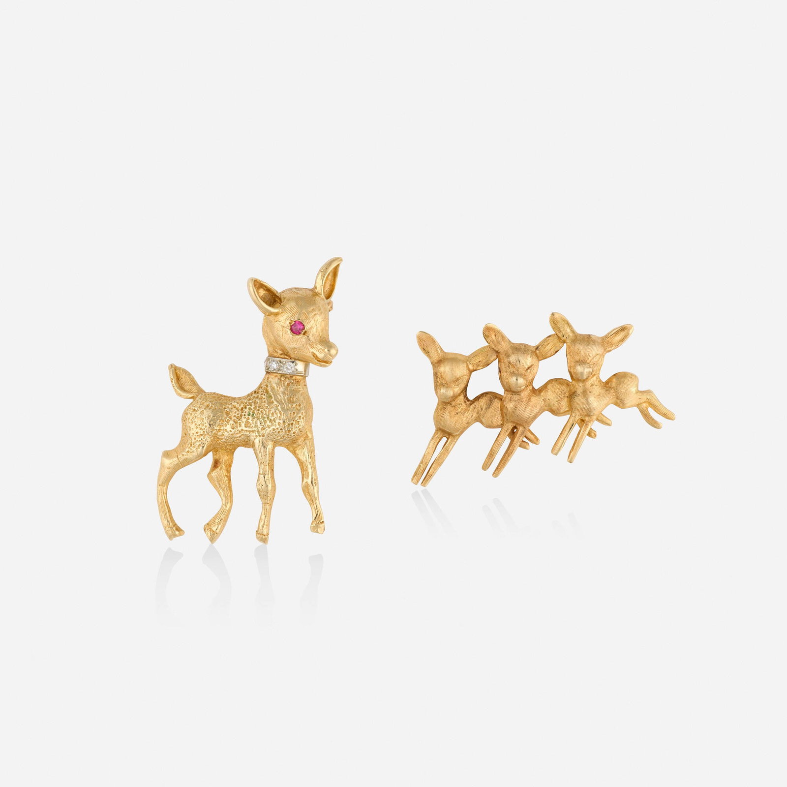 Two gold brooches: Two gold brooches One a single deer with circular-cut ruby eye and single-cut diamond collar; and one designed with three prancing deer 14k yellow and white gold 1.625 x 1 in and 1.50 x 1 in; Gross