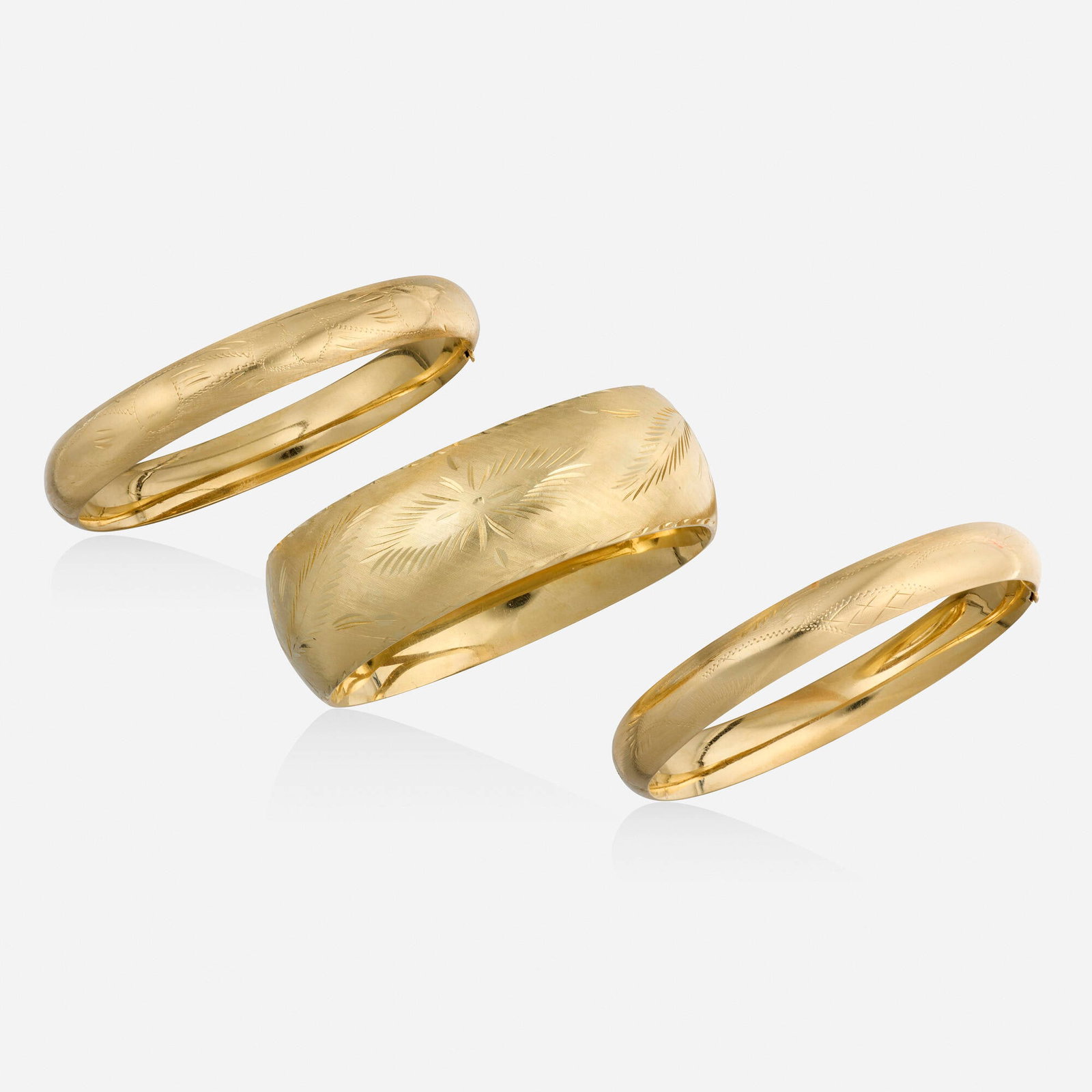 Three gold bracelets: Three gold bracelets Each hinged bangle of engraved design 14k yellow gold Inner circ. 7 in, width 0.875 in; 7.25 in, 0.375 in; 7.50 in, 0.375 in; Gross weight 42.6 dwts Provenance: Estate of Stuart