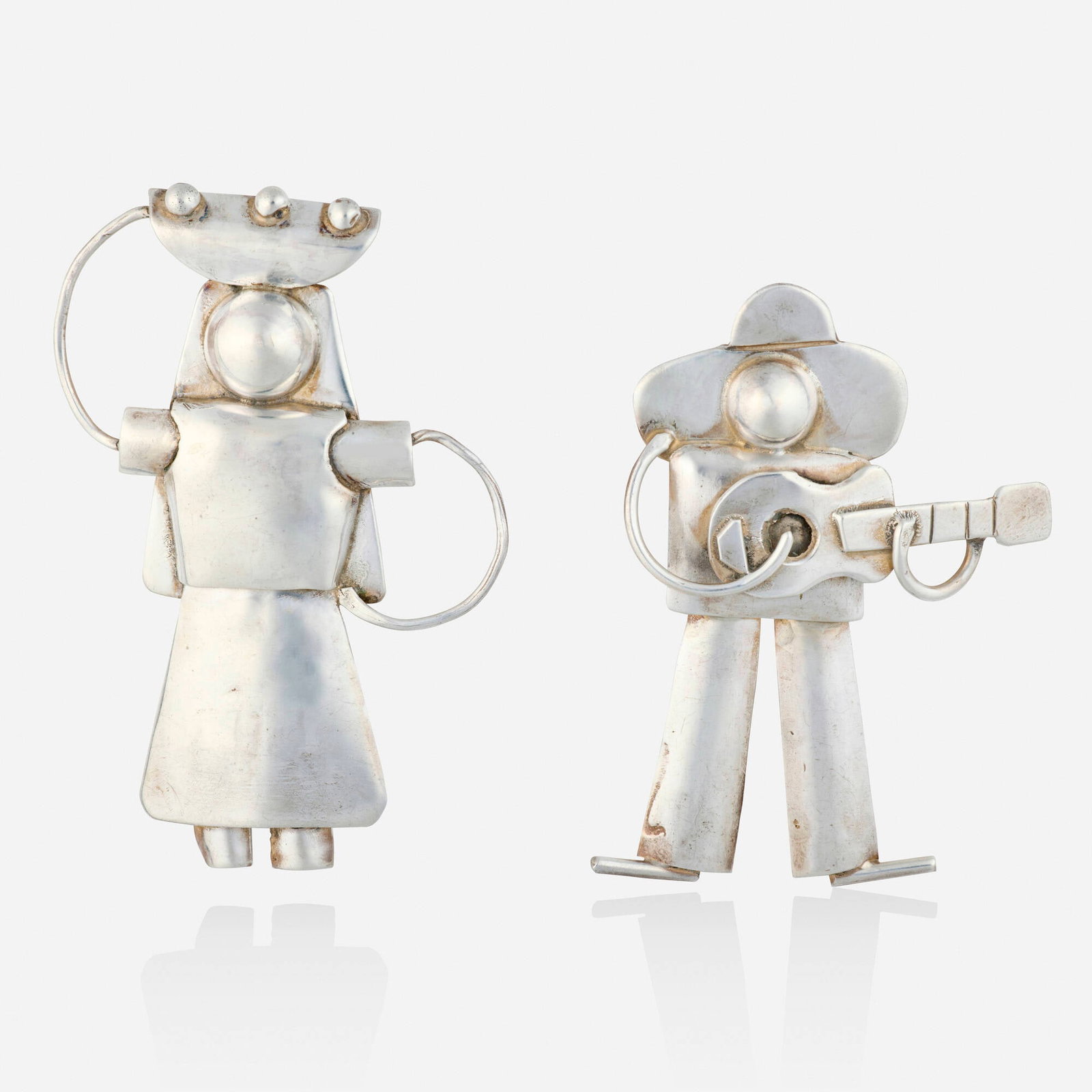Mexican, Two sterling silver brooches: Mexican Two sterling silver brooches One a male playing the guitar; one a female holding a basket Sterling silver 2.375 x 1.625 in and 2.75 x 1.875 in; Gross weight 19.5 dwts This work wil