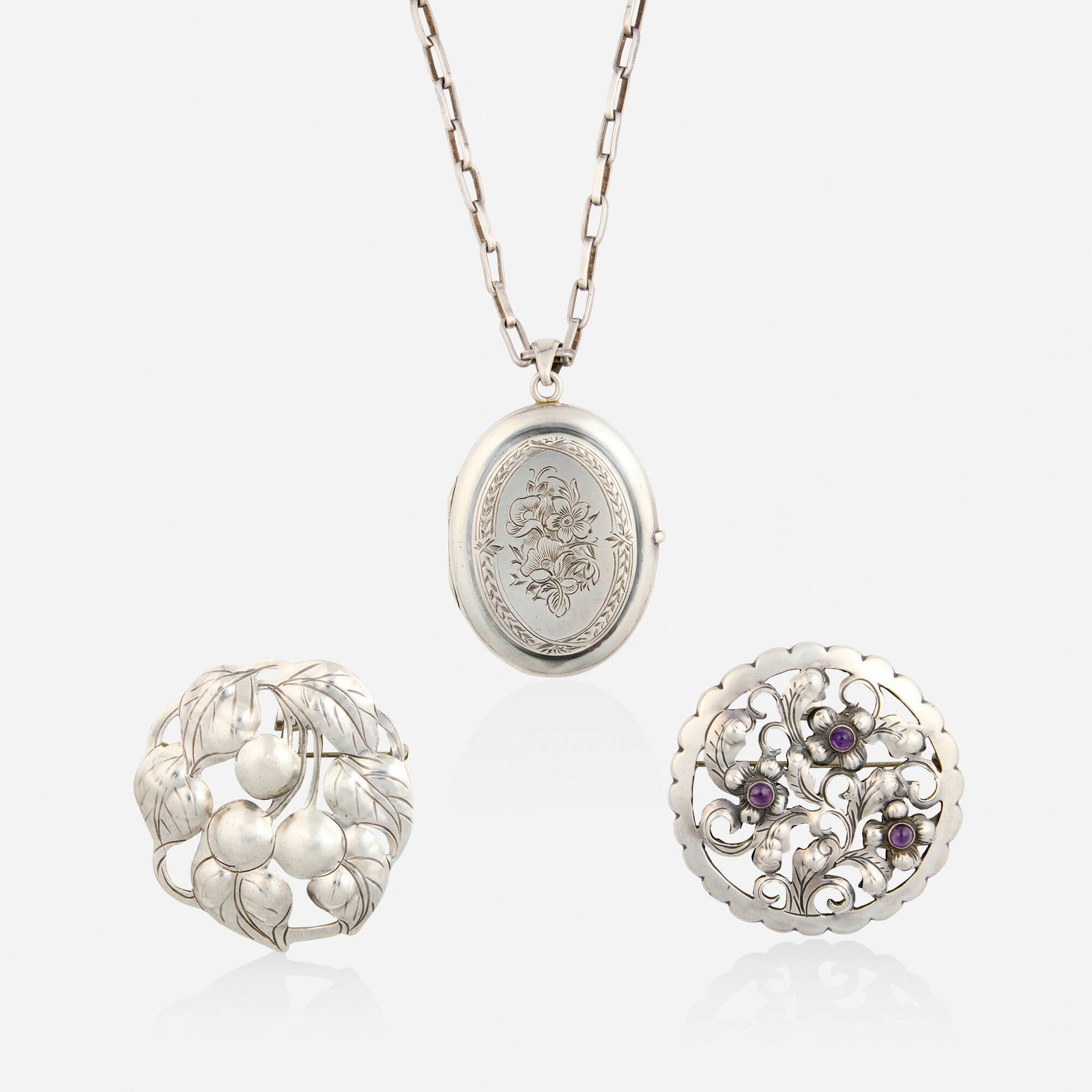 The Kalo Shop, Group of sterling silver jewelry: The Kalo Shop Group of sterling silver jewelry Comprising a floral engraved locket suspended from the chain necklace; a pendant brooch of cherry motif, no. 109; and a pendant brooch of floral design s