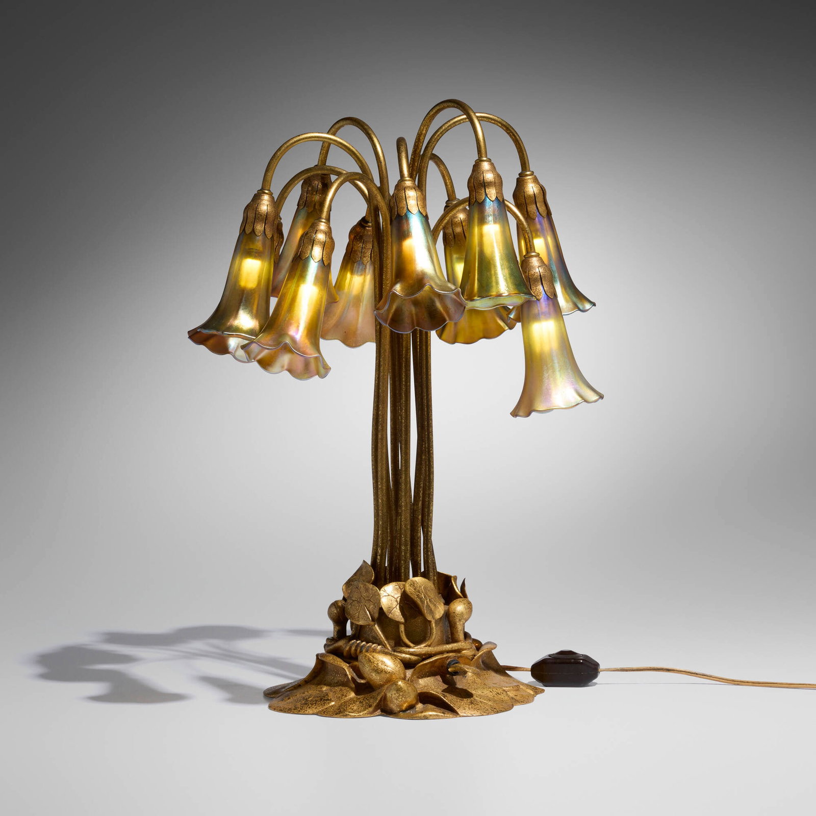Tiffany Studios, Ten-light Lily table lamp: Tiffany Studios Ten-light Lily table lamp USA, c. 1910 acid-etched and gilt bronze, hand-blown Favrile glass 20.25 h x 16 dia in (51 x 41 cm) Lamp features a Pond Lily base. Etched