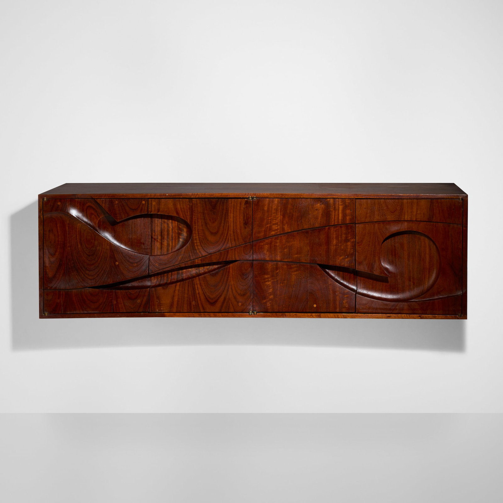 Michael Coffey, Swahili I wall-hanging cabinet: Michael Coffey Swahili I wall-hanging cabinet USA, 1972 African mozambique 25 h x 84 w x 24 d in (63 x 213 x 61 cm) Cabinet features four carved doors concealing six drawers and two adjustable