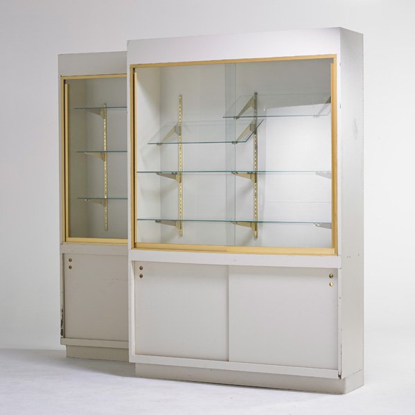 TWO STORE DISPLAY CASES: Lighting display and storage cases, USA, late 20th c. ; Laminate, lighted, sliding glass front doors with lower storage space; Each: 84" x 55 3/4" x 16"