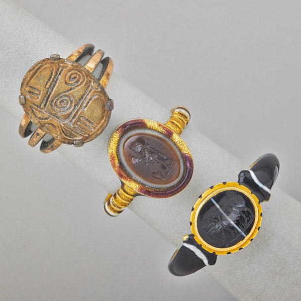 THREE ANCIENT INTAGLIO GOLD RNIGS: Hieroglyph bead on triple-shank, possibly Ancient Egyptian; Roman banded agate intaglio depicts a soldier holding a helmet; Roman banded agate intaglio with enameled hoop depicts a boar. Mounted 19th-