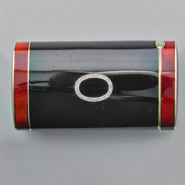 ENAMELED 14K GOLD CYLINDRICAL BOX WITH DIAMONDS: Black oval cylinder with red guilloche enamel hinged lid and base, diamond oval ornament, ca. 1930. 3". 51.8 dwt.