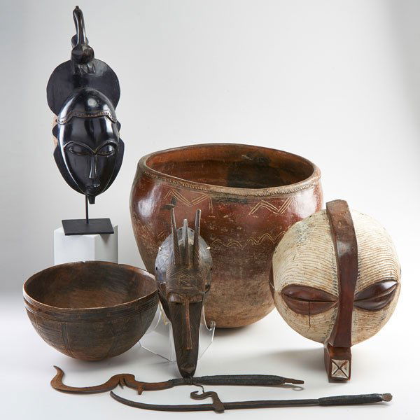 AFRICAN DECORATIVE GROUP: Seven pieces, 20th c.: West African redware bowl, three wood masks, carved wooden bowl and two iron copies of sword currency; Unmarked; Tallest: 17"