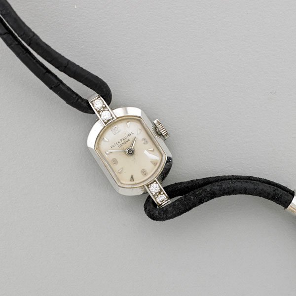 PATEK PHILIPPE LADIES PLATINUM DIAMOND WRISTWATCH: Lozenge shaped case with diamond lugs, white dial with arrow and Arabic hours, mechanical movement #947505, case #513529, Ref #3076, ca. 1960; Leather cord strap with platinum findings; Monograms; Mar