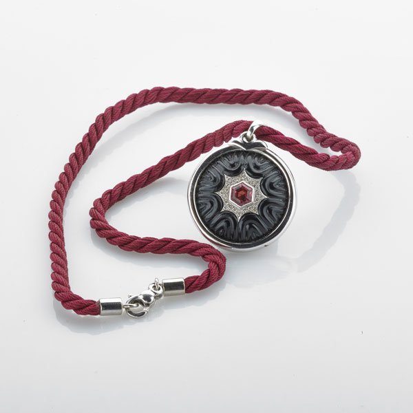 RUBELITE, CARVED ONYX AND DIAMOND MANDALA PENDANT: Bezel set hexagonal faceted rubelite with prong set diamond surround, diamonds approx. .50 ct. TW, undulating carved onyx surround, 18k wg. frame, on maroon woven silk cord with 18k wg. findings, 18";