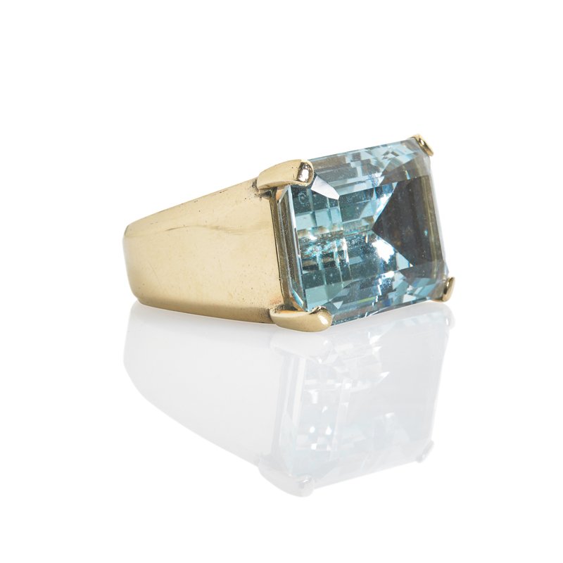MINIMALIST AQUAMARINE 14K GOLD RING: Rectangular step cut aquamarine, 22.75 x 16.65 x 11.2 mm., 31 cts. by formula, supported laterally at corners above shaped box. Unmarked. Size 6 1/2 with internal sizing hoop. 12.3 dwt.