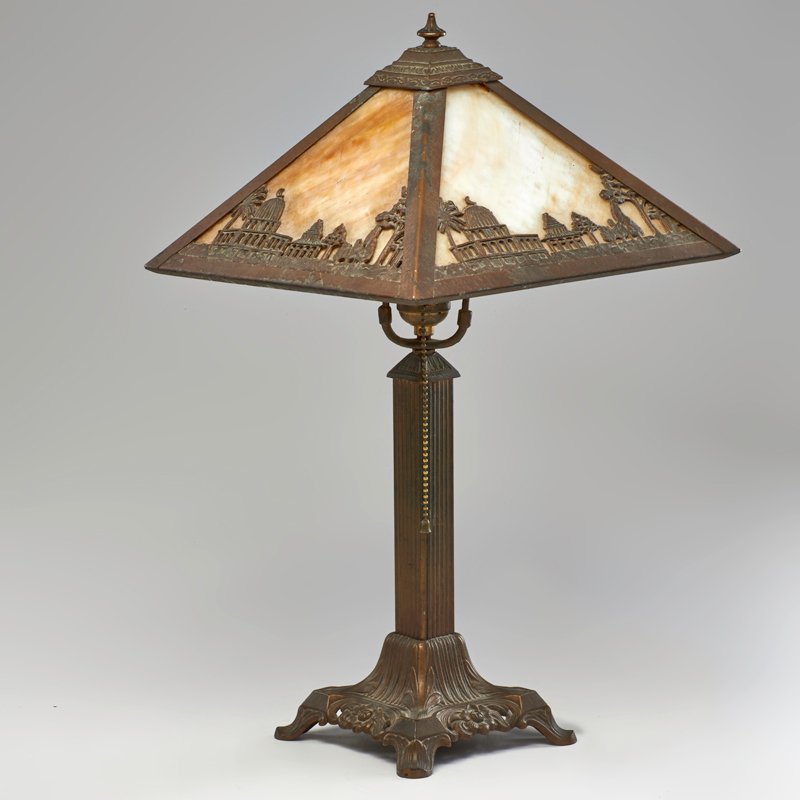 ARTS AND CRAFTS: Patinated metal table lamp with metal overlay slag glass shade decorated with Arabian scenes, USA, 1920s; To finial: 21" x 12" sq.