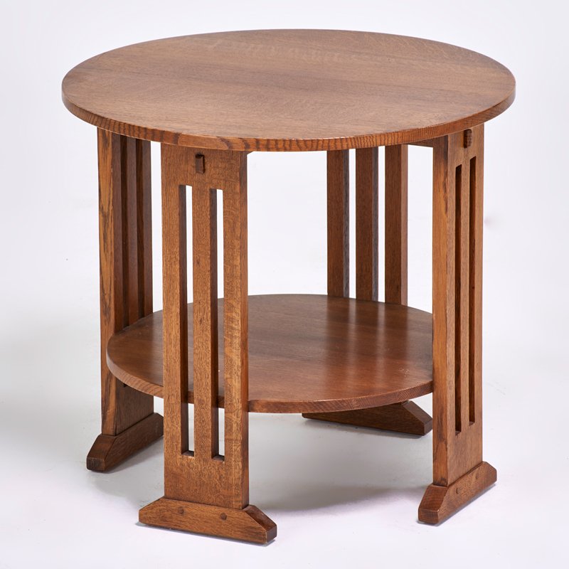STICKLEY BY E.J. AUDI: Contemporary lamp table with cut-out sides, lower shelf, and shoe feet, Manilus, NY, 2002; Quartersawn oak; Branded mark, metal tag; 24" x 26" dia.
