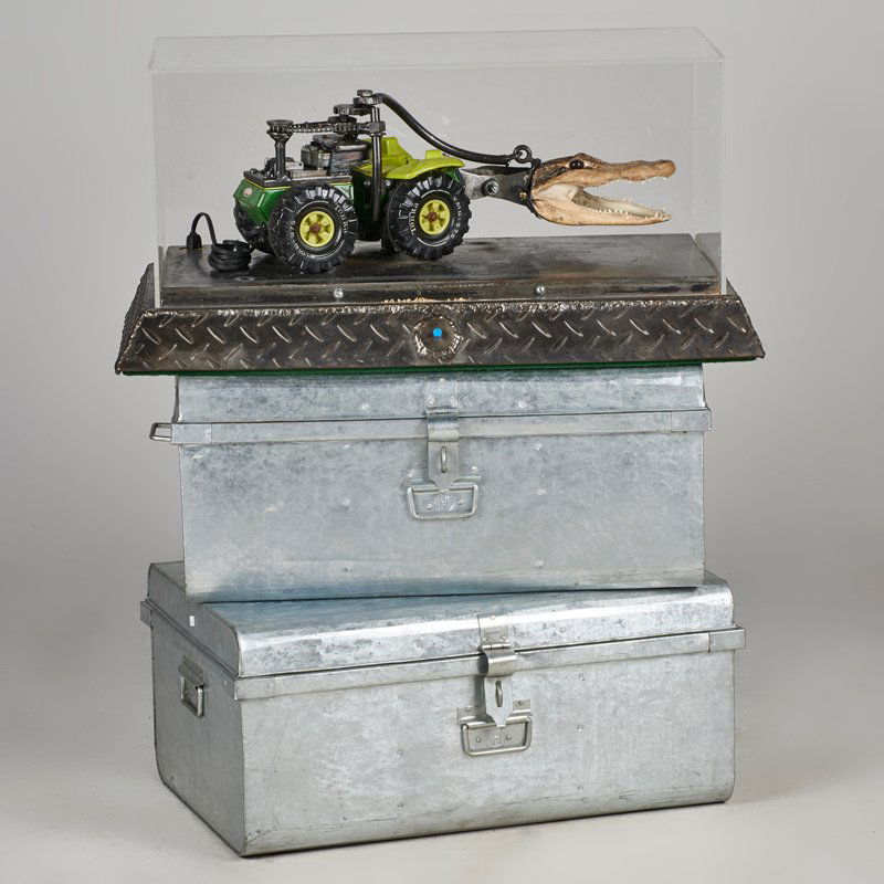 MOTORIZED CONSTRUCTION: Toy tractor with alligator skull and toy man in plexiglass box installed on two metal trunks by unknown artist; "John Carter, Warload of Mars," 1993; 15" x 23 1/4" x 17 1/2" (without trunks)