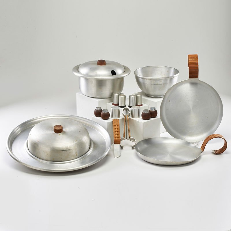 RUSSEL WRIGHT: Seventeen spun aluminum kitchen pieces: lidded tray with wooden element, two wicker-handled trays, lidded bowl with wooden element, deep bowl, four salts, two pairs of salt and peppers, wickered chees