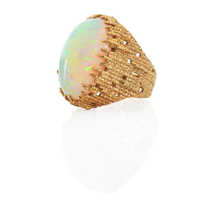 ANDREW GRIMA OPAL & GOLD RING: An oval gray opal cabochon, 12.4 cts. by formula, set in textured 18k yellow gold. London, ca. 1970. Interior tag marked Grima AG LTD. Size 4. 10 dwt. Provenance: From a Chicago Estate.