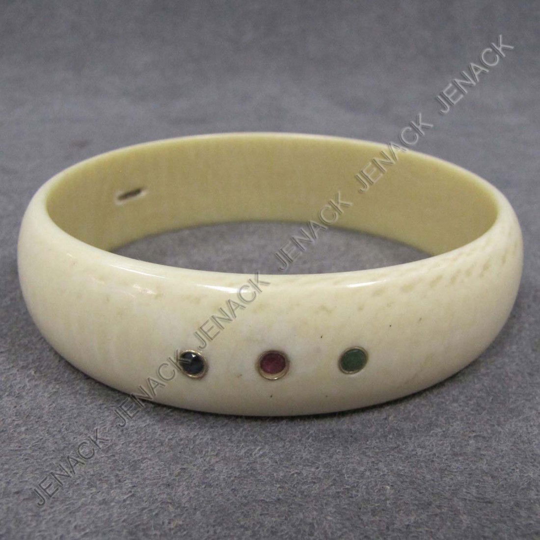 CARVED ELEPHANT IVORY BANGLE: CARVED ELEPHANT IVORY BANGLE 14K BEZEL SET WITH (2) SAPPHIRE, (2) RUBY, AND (1) EMERALD (1/EMERALD MISSING). DIAMETER 2 3/4" **CANNOT EXPORT IVORY**