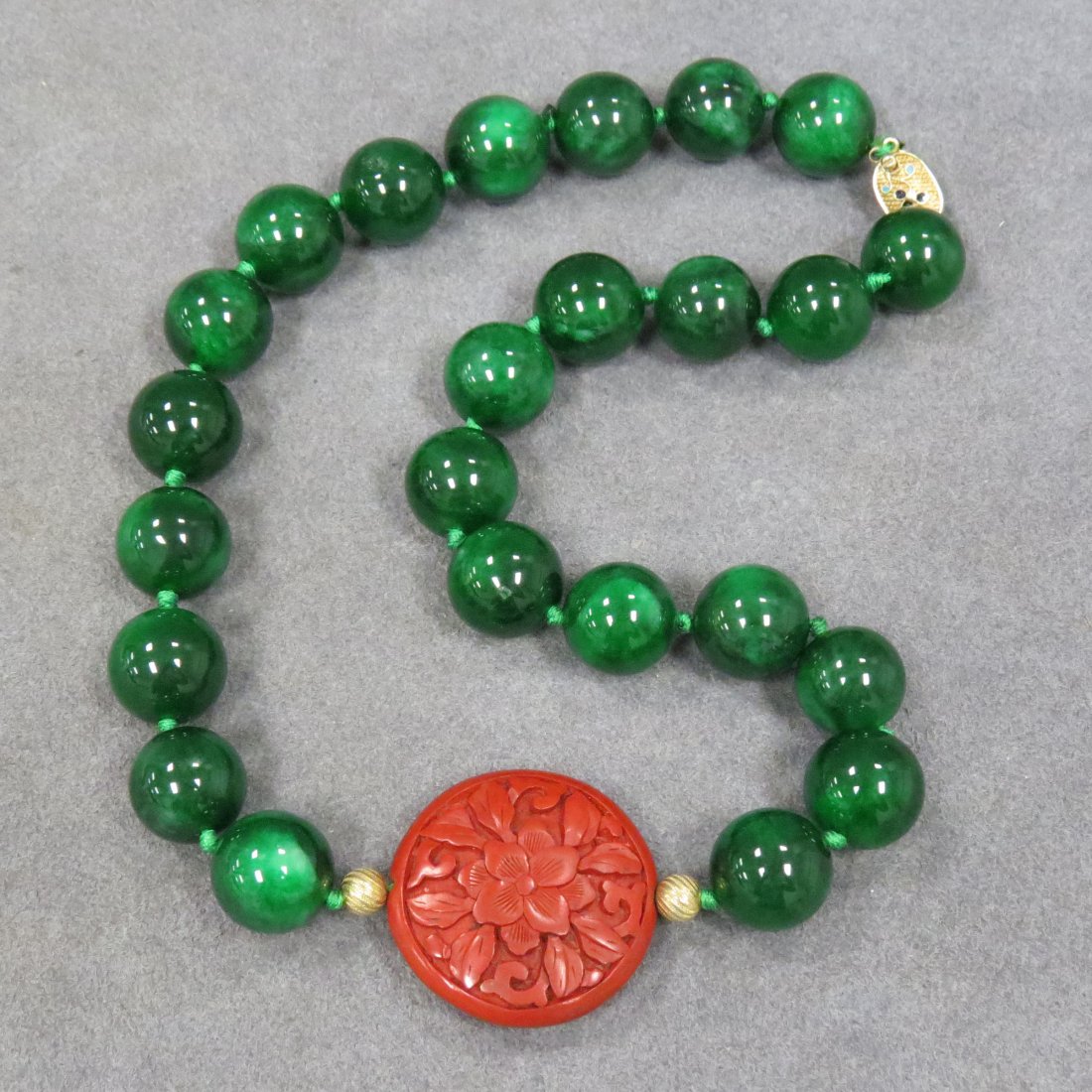 STRAND NECKLACE WITH GREEN HARDSTONE BEADS: STRAND NECKLACE WITH GREEN HARDSTONE BEADS, APPROXIMATE 15.9MM AND CARVED CINNABAR WITH GILT SILVER CLASP. LENGTH 19"