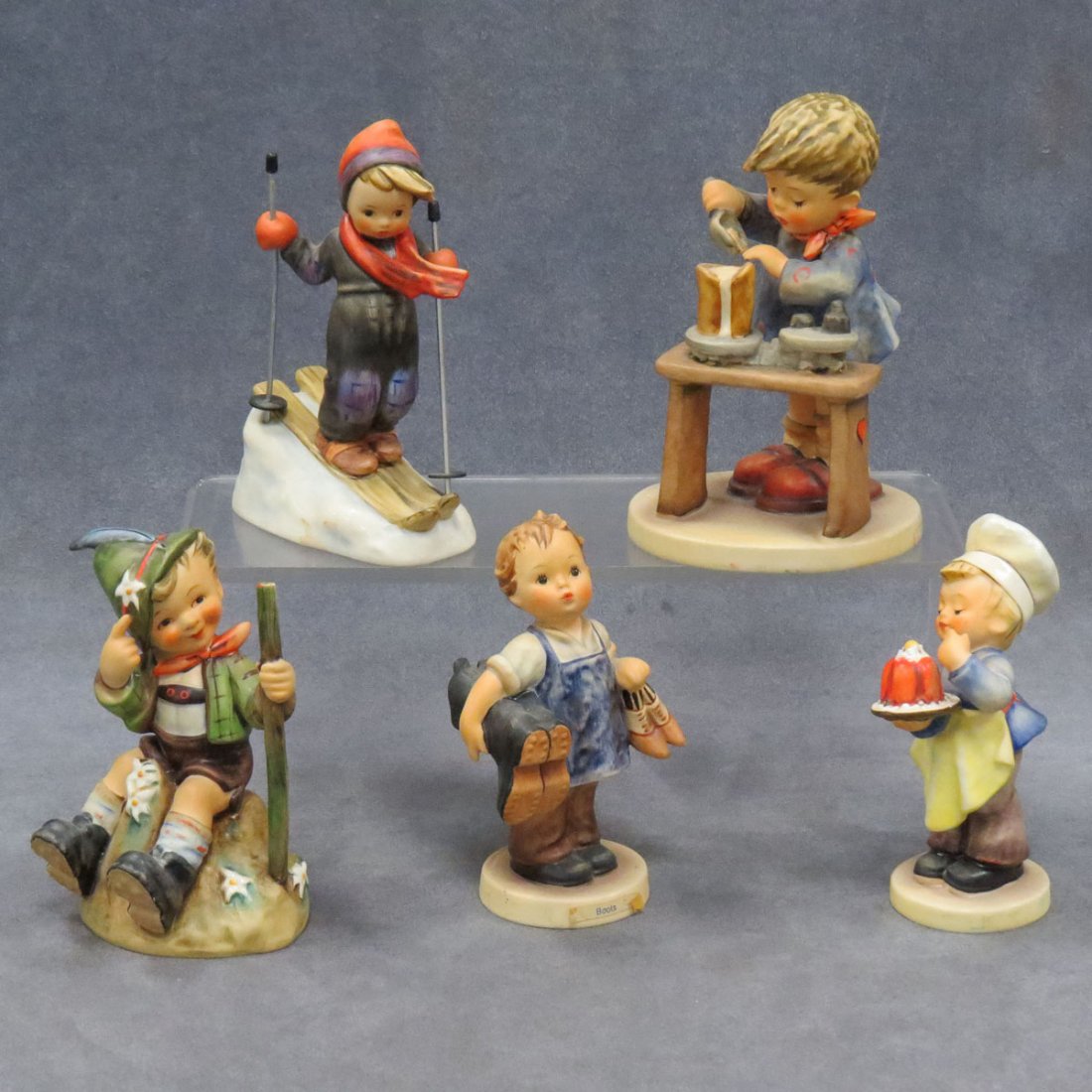 LOT (5) GOEBEL HUMMEL FIGURES: LOT (5) GOEBEL HUMMEL FIGURES, TMK-5 AND TMK-6 MARKS INCLUDING BOOTS, #143, HEIGHT 5"; BAKER, #128, HEIGHT 5"; SKIER, #39, HEIGHT 5"; MOUNTAINEER, #315, HEIGHT 5 1/4"; A FAIR MEASURE, #345, HEIGHT 6"