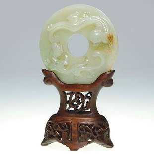 Carved Jade bi disc,dragons,wood stand,4 5/8: Jade bi disc with light brown inclusions, one side carved with a pair of dragons. The disc measures 2 5/8 inch and is lofted upon a neatly carved openwork wood stand with dark stain. Combined height i