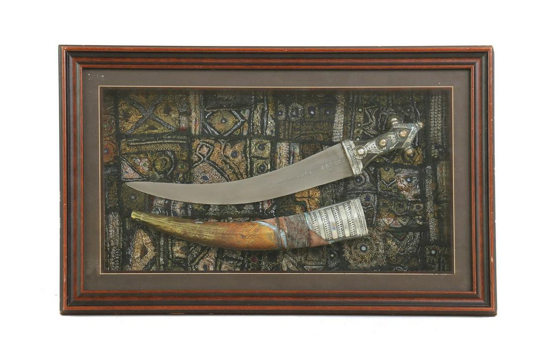 A framed Bedouin jambiya and sheath: A framed Bedouin jambiya and sheath A framed Bedouin jambiya and sheath, late 19th early 20th century, Asir with brass pierced and engraved fittings in presentation box 44.5cm x 71cm the frame the bla