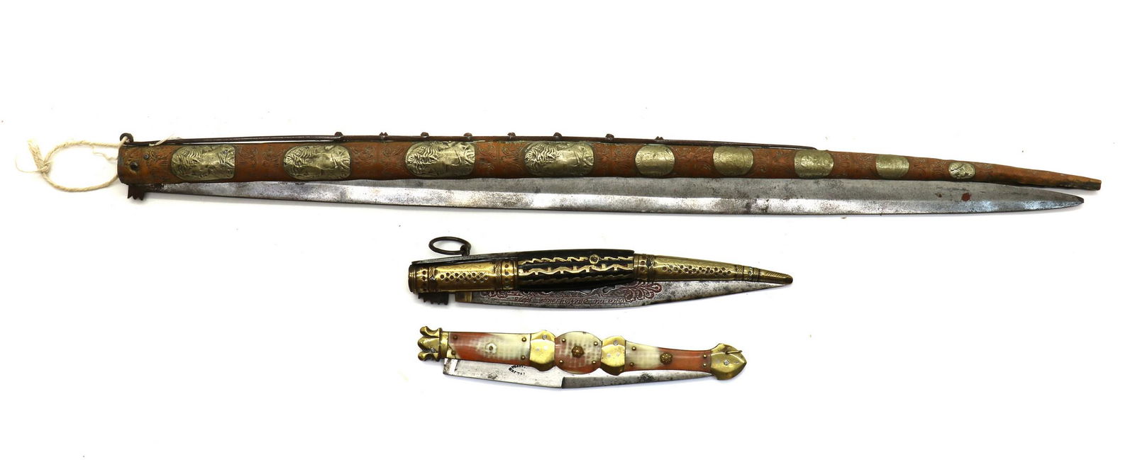 A large Spanish folding Navaja and another (2): A large Spanish folding Navaja and another (2) A large Spanish folding Navaja, late 19th century, with a sprung loaded 64cm single edged blade, the tapering brass covered rounded wood handle engraved
