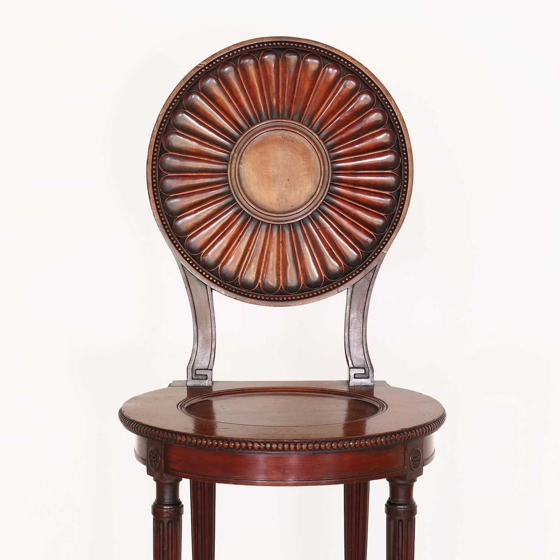 A George III mahogany hall chair by Thomas Chippendale,: A George III mahogany hall chair by Thomas Chippendale, A George III mahogany hall chair by Thomas Chippendale, c.1775, the circular patera-carved back with beaded detail, above a dished seat and a pl