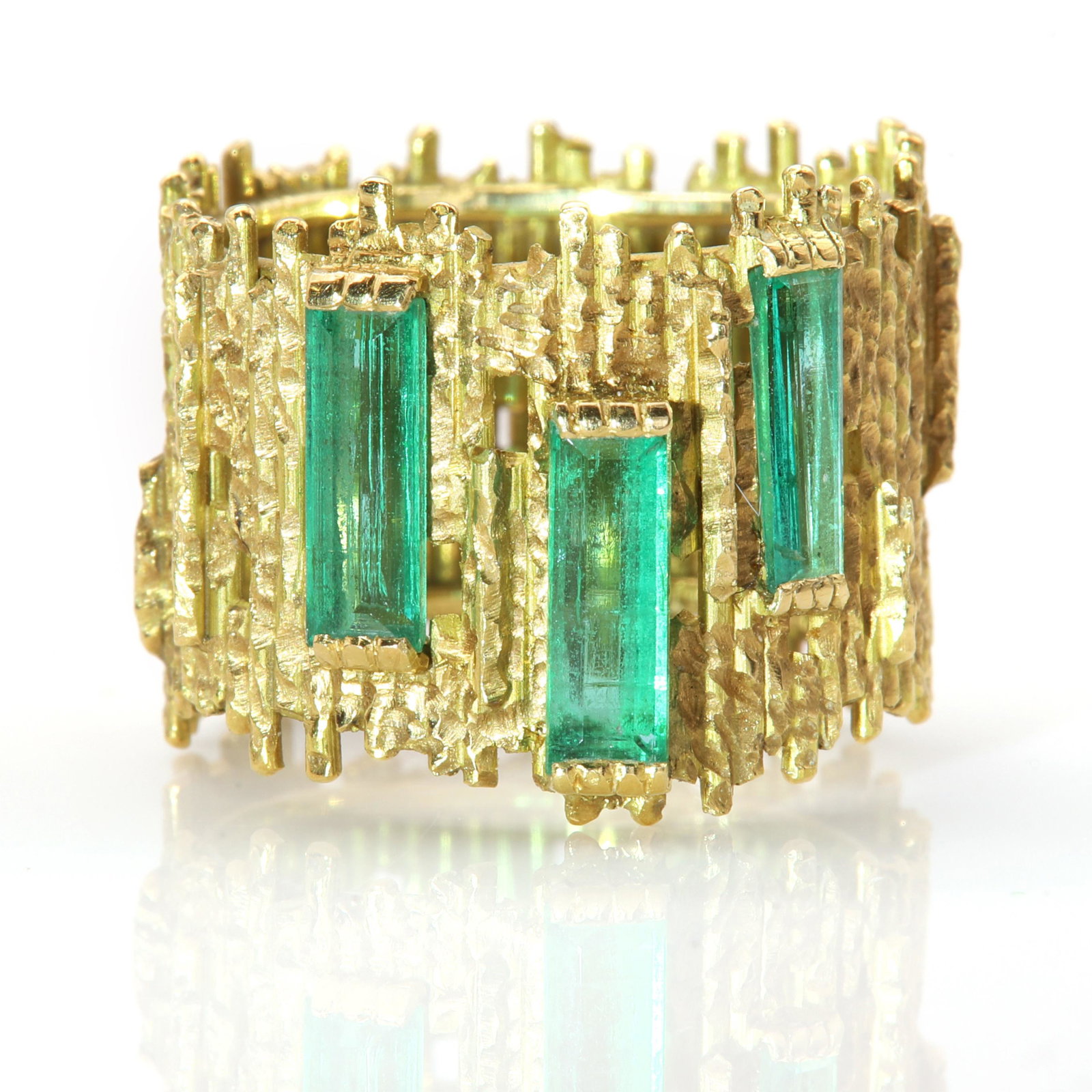 An 18ct gold emerald ring, by Andrew Grima, c.1960,: An 18ct gold emerald ring, by Andrew Grima, c.1960, An 18ct gold emerald ring, by Andrew Grima, c.1960, with three elongated trap cut emeralds, end set in a staggered position. A flat section shank co