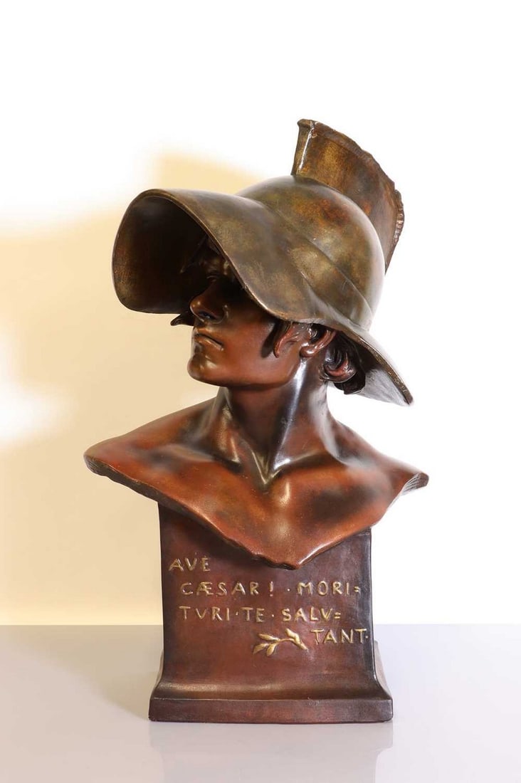 A Goldscheider cold-painted terracotta bust,: A Goldscheider cold-painted terracotta bust, A Goldscheider cold-painted terracotta bust, c.1900, modelled as a gladiator in a helmet, raised on an integrated socle with motto 'Ave Cesar! Morituri te