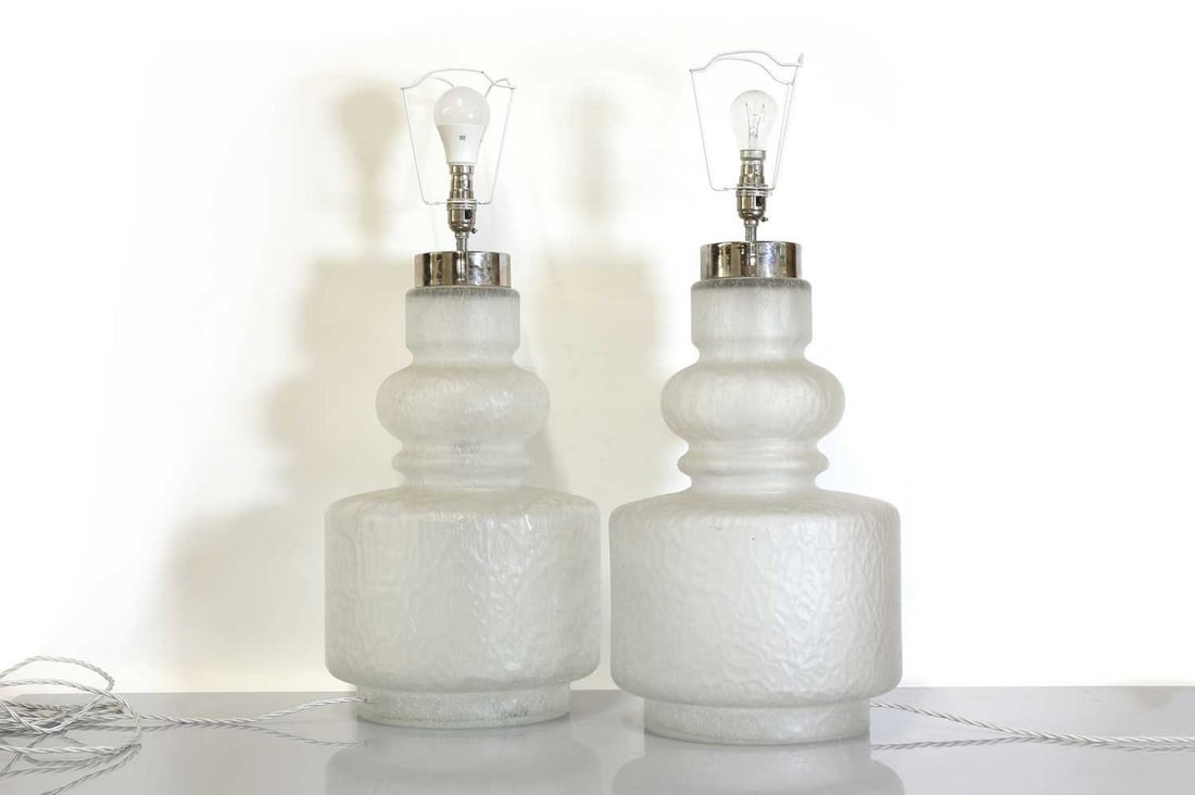 A pair of moulded glass table lamps,: A pair of moulded glass table lamps, A pair of moulded glass table lamps, 1970s, in the manner of Holmegaard, each frosted body of stepped form, with chromed fittings for two bulbs, with a pleated fab