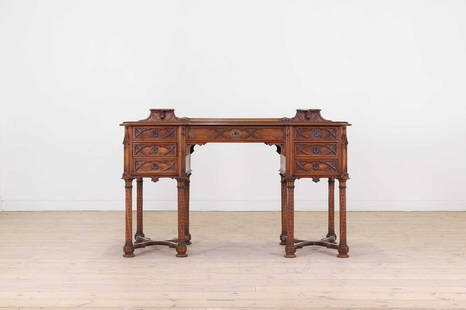 A late Victorian Gothic Revival walnut desk: A late Victorian Gothic Revival walnut desk A late Victorian Gothic Revival walnut desk, late 19th century, the rectangular top with a raised gallery and a leather surface, above an arrangement of sev