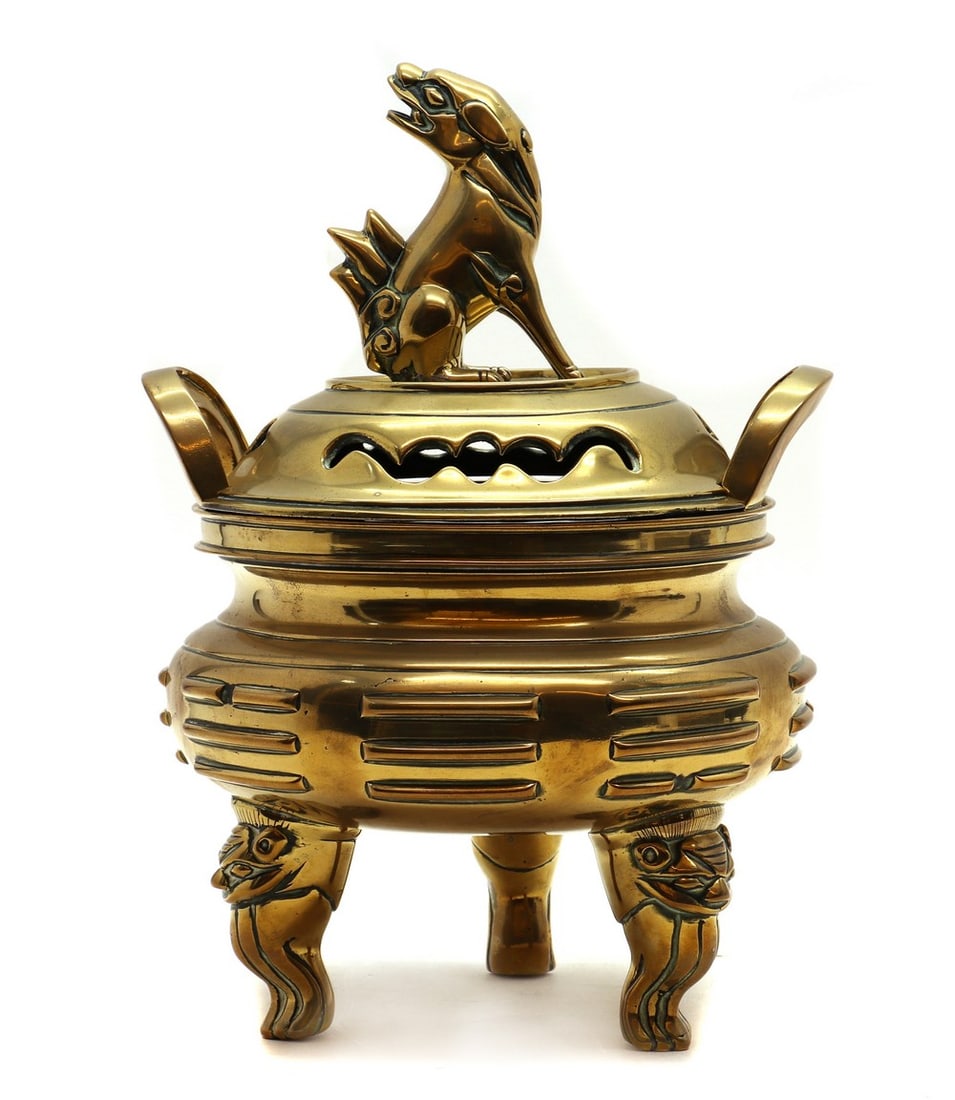 A Chinese brass incense burner: A Chinese brass incense burner A Chinese brass incense burner, 20th century, of circular form, the cover pierced and with figural surmont, the twin-handled reeded base raised on three mask and claw fe