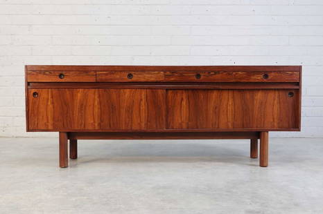 An Archie Shine rosewood sideboard,: An Archie Shine rosewood sideboard, 1970s, designed by Robert Heritage (1927-2008), retailed by Heal's, with four parallel frieze drawers, each with recessed handles, over a pair of sliding doors, ope