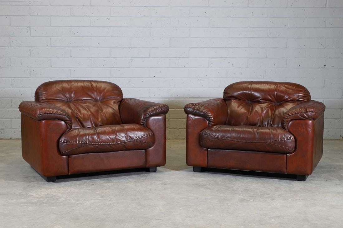 A pair of Swiss De Sede 'DS101' reclining armchairs,: A pair of Swiss De Sede 'DS101' reclining armchairs, 1970s, each upholstered throughout in chestnut leather, with wide stitched detailing to the edges of all cushions, 109cm wide 102cm deep 73cm high,