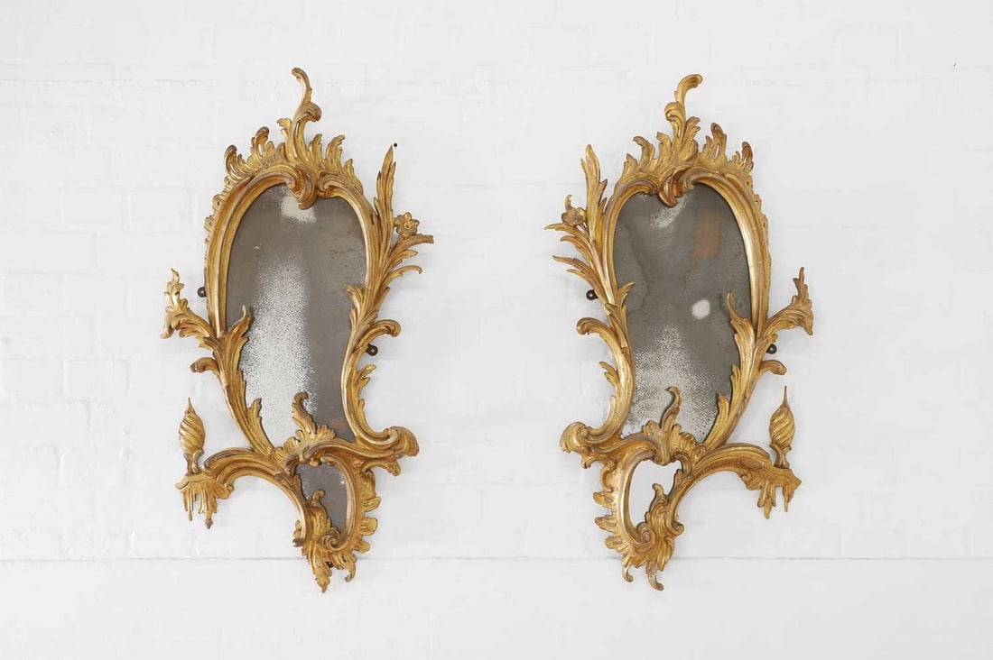 A pair of George III carved giltwood girandoles, after a design by Thomas Chippendale,: A pair of George III carved giltwood girandoles, after a design by Thomas Chippendale, c.1760, each shaped mirror plate within an asymmetrical frame of moulded acanthus scrolls, and issuing a flame fi