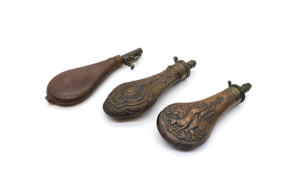 Two powder flasks,: Two powder flasks, 19th century, comprising two examples in copper, one with embossed a hare and game birds 21.5cm high, the other embossed with a foliate decoration 22cm high, together with a leather