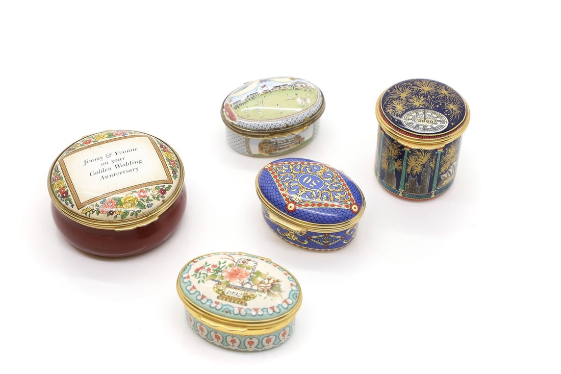 A group of five Halcyon Days enamel pill boxes,: A group of five Halcyon Days enamel pill boxes, to include a Millennium example 4.5cm high, '1992' 5.5cm wide, '50' 5.5cm wide, together with another depicting a cricket match 5.5cm wide, and a person