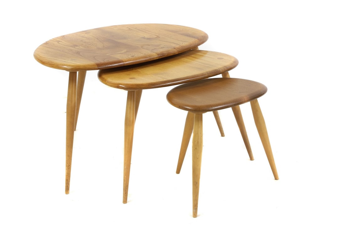An Ercol nest of three beech 'Windsor' pebble tables,: An Ercol nest of three beech 'Windsor' pebble tables, each with tapered legs, 65cm, 49cm, 34cm wide 39.5cm high Condition Report: Smaller table darker than the others. Good overall. Blue label to smal